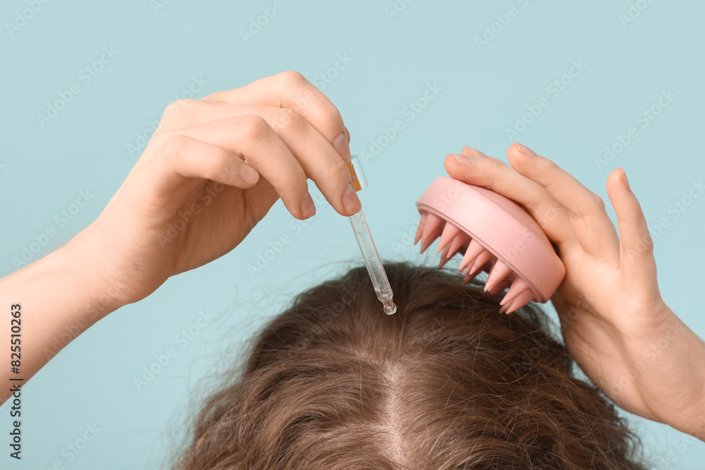 Naklejka premium Young woman using hair scalp massager with cosmetic oil on blue background, closeup