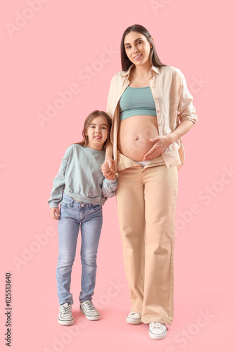 Little girl with her pregnant mother holding hands on pink background
