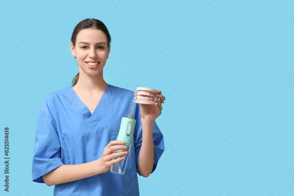 Female dentist with oral irrigator and jaw model on blue background Female dentist with oral irrigator and jaw model on blue background