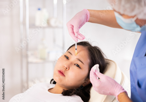 Closeup face of young female client receiving injections during lip enhancement procedure, professional cosmetologist hands in rubber gloves holding syringe