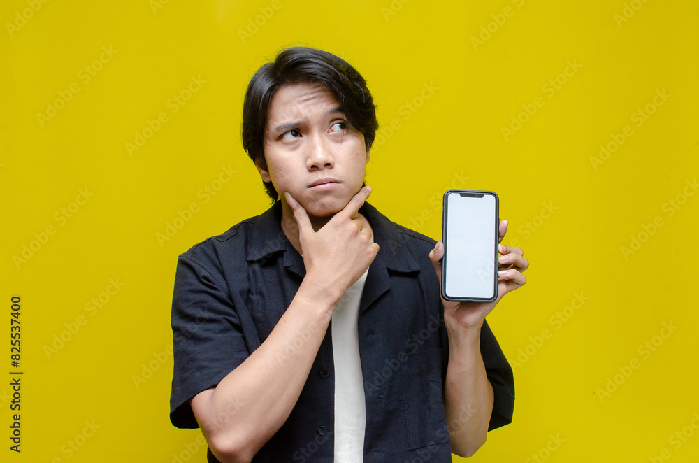 an overthinker young asian man thinking deeply while showing his screen phone after receiving bad news. thoughtful asian man showing his blank screen phone an overthinker young asian man thinking deeply while showing his screen phone after receiving bad news. thoughtful asian man showing his blank screen phone
