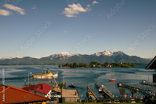 Blick über den Chiemsee mit Fraueninsel, schneebedeckten Bergen und einem Dampfer 