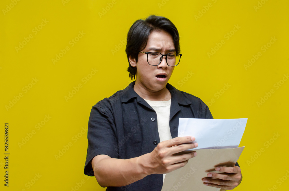 asian man opening envelope receiving and reading bad news letter. An angry man is upset over his excessive expenses, notice of termination, bank debt, and tax invoice. asian man opening envelope receiving and reading bad news letter. An angry man is upset over his excessive expenses, notice of termination, bank debt, and tax invoice.