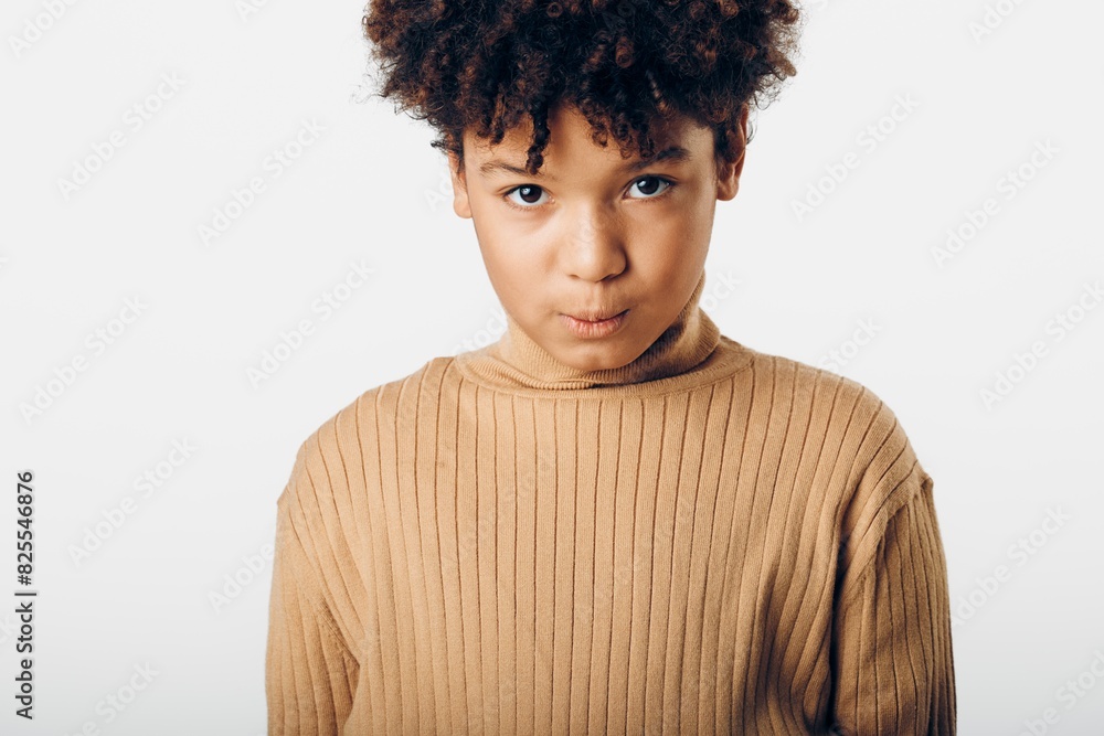 Confident young african american boy with expressive afro hair gazing intently at camera against a clean white background Confident young african american boy with expressive afro hair gazing intently at camera against a clean white background