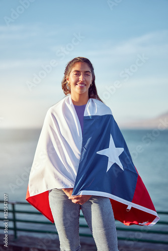 cheerful chilean woman holding over the shoulders a flag of Chile outdoors against blue sky and ocean, celebration and patriotism concept	