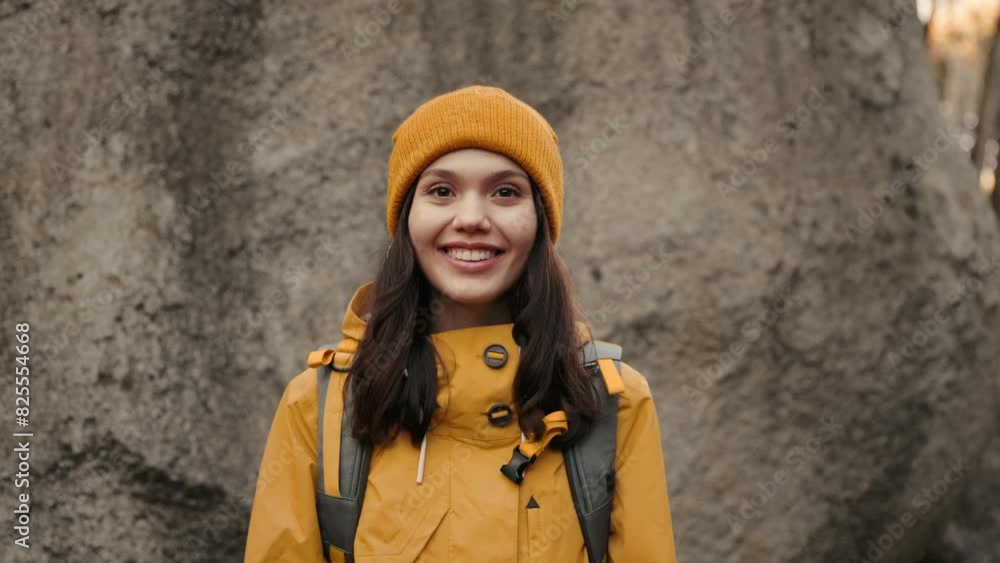 Smiling young female in stylish yellow jacket and orange beanie posing outdoors with a content expression, showcasing casual fall fashion. Smiling young female in stylish yellow jacket and orange beanie posing outdoors with a content expression, showcasing casual fall fashion.
