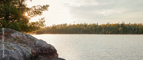 фотографія Sunrise behind rocks and pines on a boundary waters lake during autumn