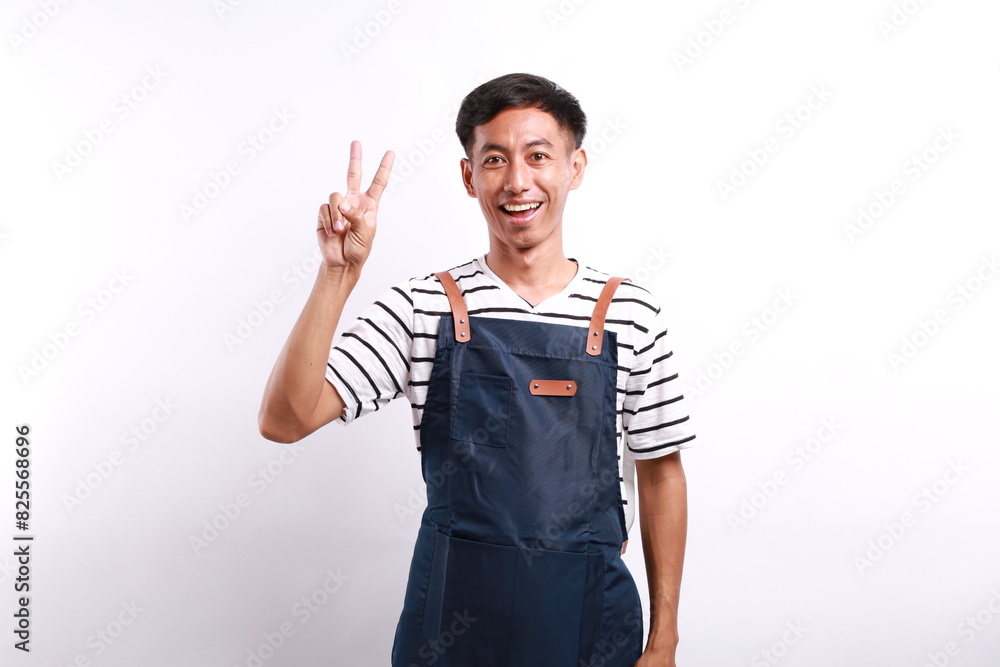Asian young man wearing apron over white background showing two fingers with exited and happy face expression Asian young man wearing apron over white background showing two fingers with exited and happy face expression