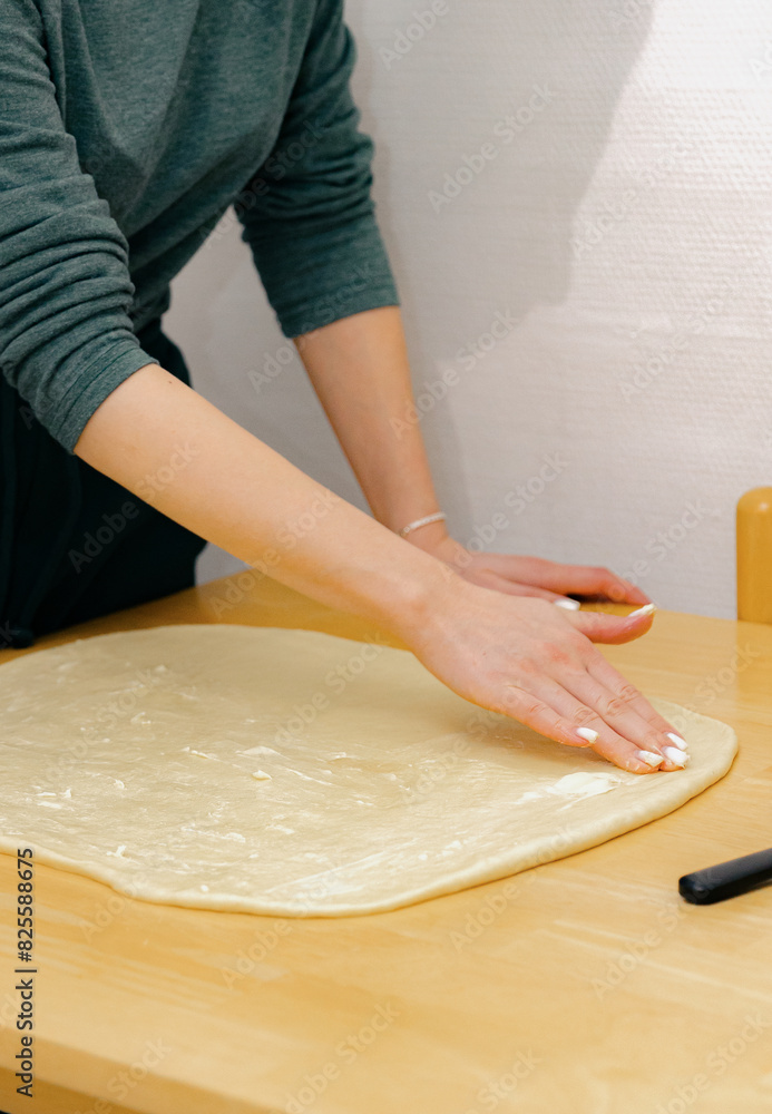 One Caucasian young girl greases the dough on the table with butter.