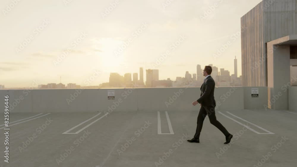 Businessman in formal attire walks alone on a rooftop parking deck, with the urban skyline at sunset in the background. He carries a bag, creating a solitary yet professional scene. Slow motion. Businessman in formal attire walks alone on a rooftop parking deck, with the urban skyline at sunset in the background. He carries a bag, creating a solitary yet professional scene. Slow motion.