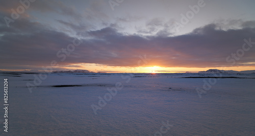 Orange Sunset with sun rays under clouds on snowy plain