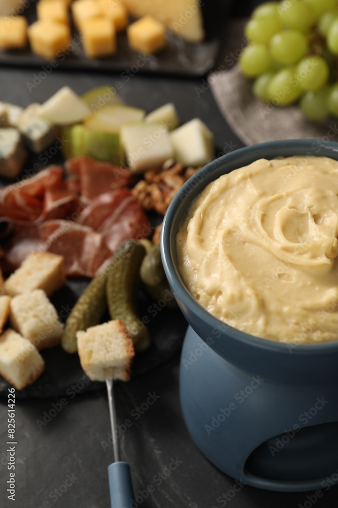 Fondue with tasty melted cheese, fork and different snacks on black table Fondue with tasty melted cheese, fork and different snacks on black table