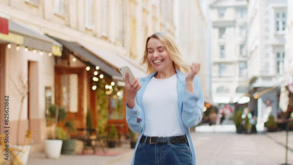 Caucasian young woman using mobile smartphone celebrating win good message news, lottery jackpot victory, giveaway online outdoors. Happy adult lady tourist standing in city street. Town lifestyles Caucasian young woman using mobile smartphone celebrating win good message news, lottery jackpot victory, giveaway online outdoors. Happy adult lady tourist standing in city street. Town lifestyles