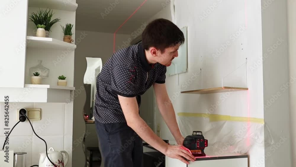 A young man checks the levelness of a shelf with a laser level. A young man checks the levelness of a shelf with a laser level.