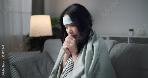 Footage dolly shot, Unwell young woman have a high fever feel chills ,wrapped in blanket sitting on sofa in the living room at home, healthcare woes photo