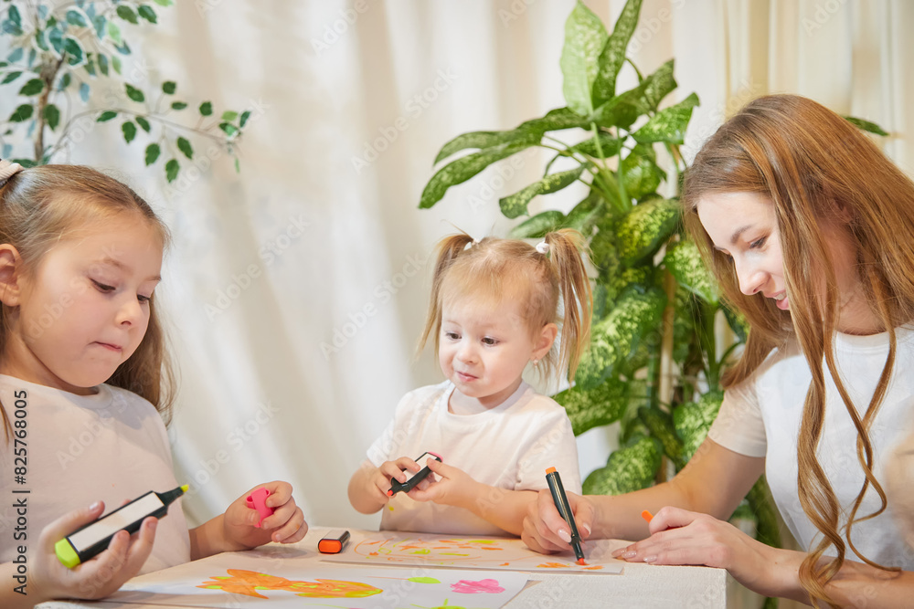 Obraz premium Young mother or babysitter, little daughter, sister teenager girl drawing at table in room. Painting, doing homework, family enjoying leisure at home