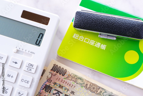 テーブルの上に置かれた銀行の預金通帳と印鑑、1万円札、電卓
 photo