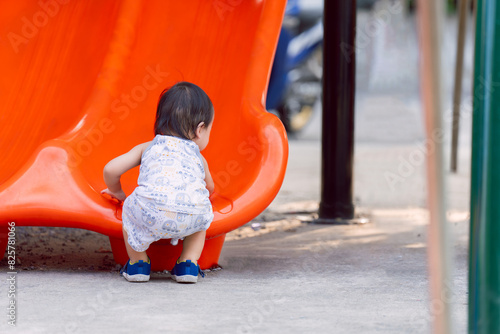 The back of a toddler son is having fun climbing an orange slide, in the summer or spring time, developing muscles and being physically active. A boy aged one year and six months. Happy playing time. © Kanthita