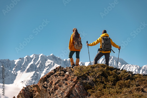 Two active hikers or tourists with backpacks are standing on view point with a great view at white mountains with glaciers