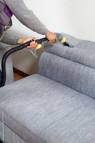 vertical shot of A man is cleaning a couch with a steam cleaner.
