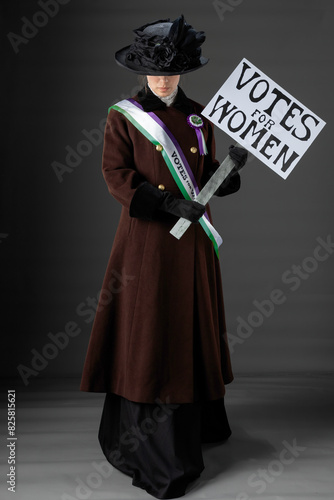 United Kingdom Victorian or Edwardian Suffragette wearing historically accurate purple and green sash and rosette against a plain studio backdrop