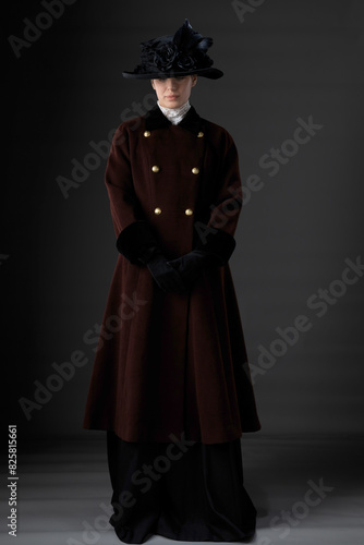 A Victorian or Edwardian woman wearing a winter coat and hat against a studio backdrop