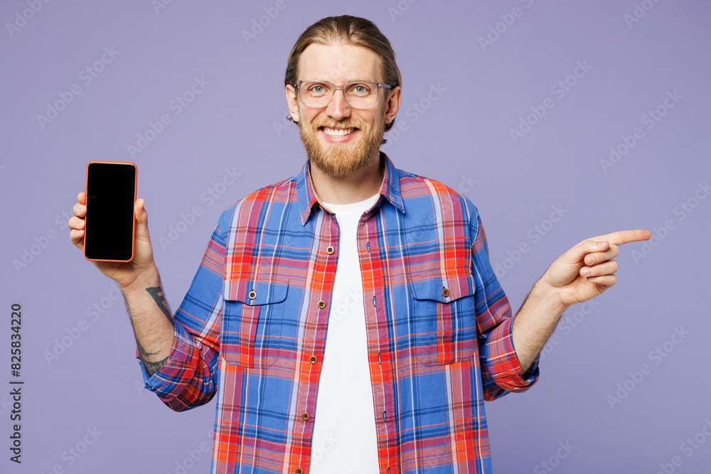 Young happy man he wear blue shirt casual clothes hold in hand use blank screen workspace area mobile cell phone point finger aside isolated on plain pastel light purple background. Lifestyle concept. Young happy man he wear blue shirt casual clothes hold in hand use blank screen workspace area mobile cell phone point finger aside isolated on plain pastel light purple background. Lifestyle concept.