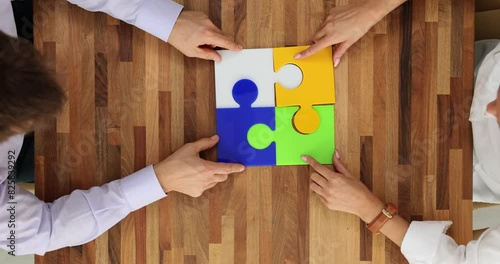 Four hands of business people collect colorful puzzle pieces on wooden table photo