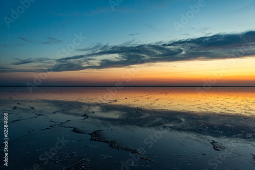 Sunset or sunrise on salt lake Elton  Russia  with mirror or reflection of high Altocumulus or Cirrocumulus clouds in the brine at golden hour. Evening or morning. Volrograd district.