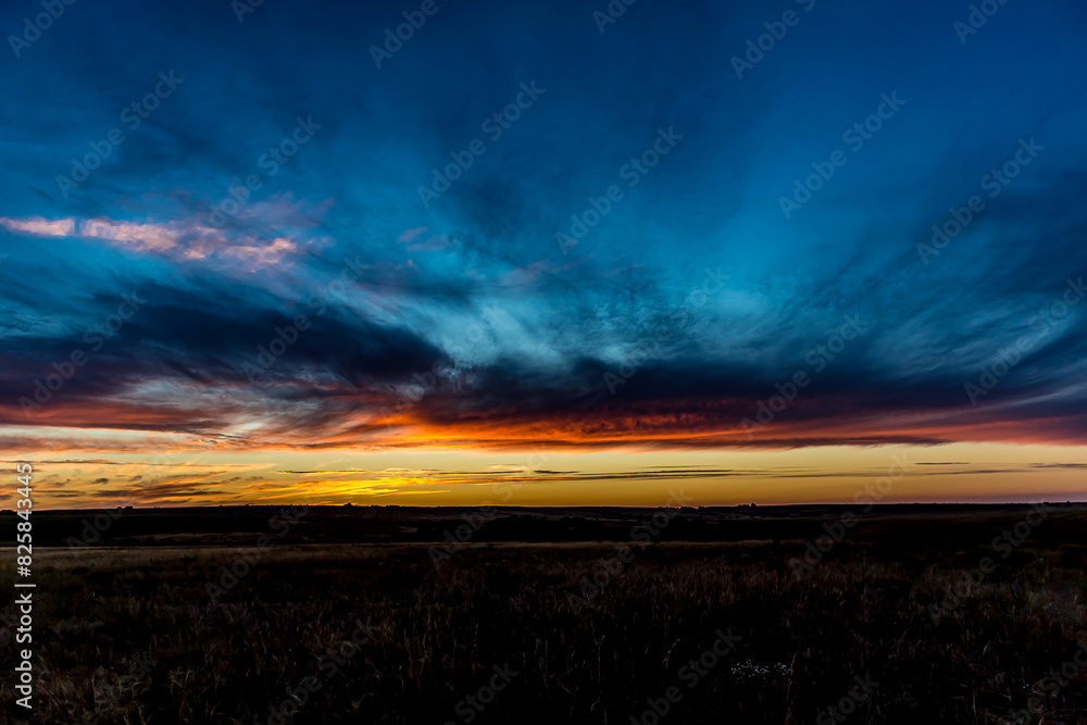 Fototapeta premium Sunrise or sunset in the Russian steppe at golden hour. Stratus, Cirrocumulus and Altocumulus clouds. The sun is shining from behind a cloud. Red orange and white shades. Morning or evening.