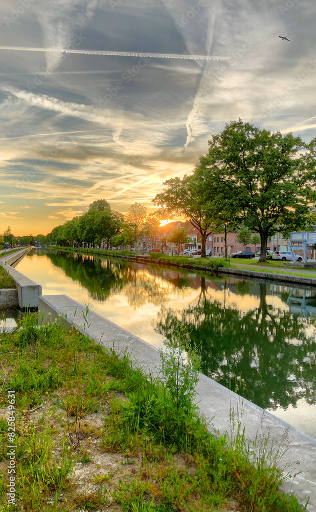 Urban canal, treelined, reflects stunning sunset sky with contrails, creating peaceful outdoor landscape