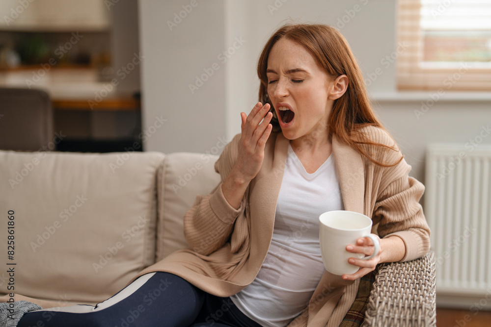 redhead woman yawning drinking coffee tea sitting on sofa at home redhead woman yawning drinking coffee tea sitting on sofa at home