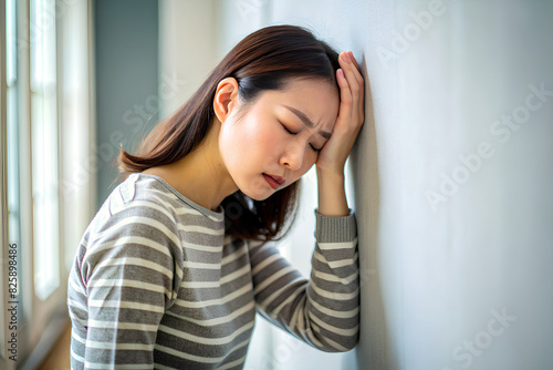young woman, headache or migraine pain. suffering from vertigo, difficulty standing up leaning on wall at home, holding head with hand