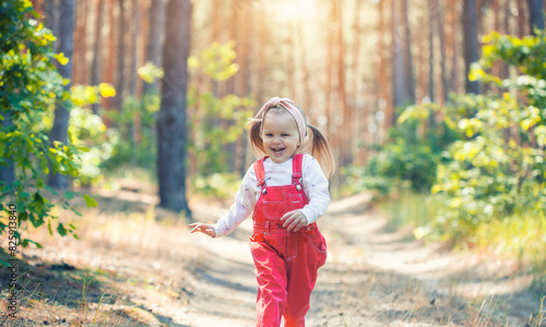 Portrait of smiling three years old caucasian child girl runs on the trail in the pine forest. Waving hands. Forest on bright light background.