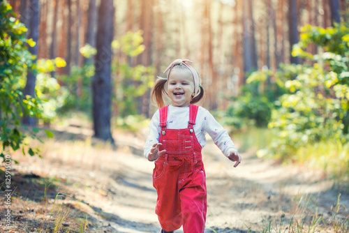 Portrait of smiling three years old caucasian child girl runs on the trail in the pine forest. Waving hands. Forest on bright light background.
