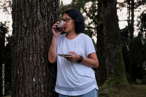 A woman was leaning against a tree trunk while drinking a cup of chocolate photo