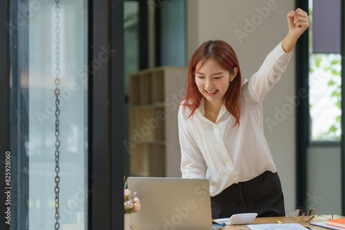 Asian businesswoman cheering while working on a laptop in an office.