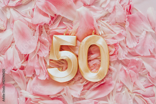 Number fifty 50 golden celebration birthday candle on pink flower petals Background. fifty years birthday. concept of celebrating birthday, anniversary, important date, holiday