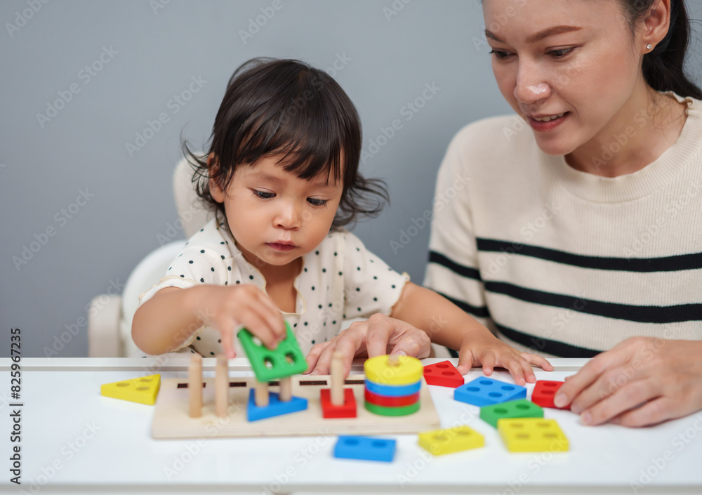 mother teaching her toddler baby girl to playing wooden educational geometric on table mother teaching her toddler baby girl to playing wooden educational geometric on table