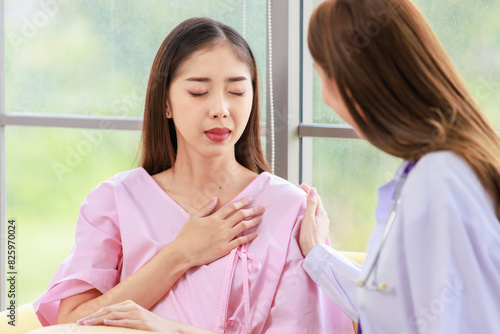 Asian young woman doctor smiling caring supporting touching mature shoulder of female patient sitting on sofa at clinic or hospital. Medicine, healthcare and help people concept