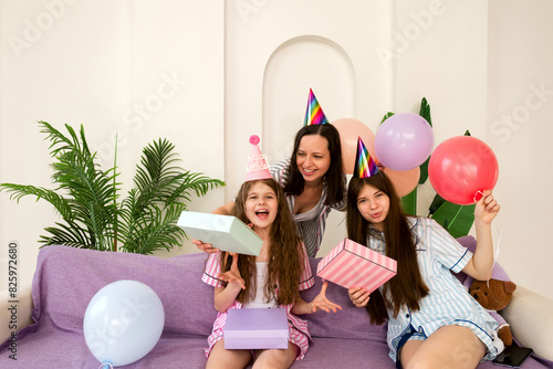Joyful birthday celebration with mother and daughters opening gifts. (ID: 825972680)
