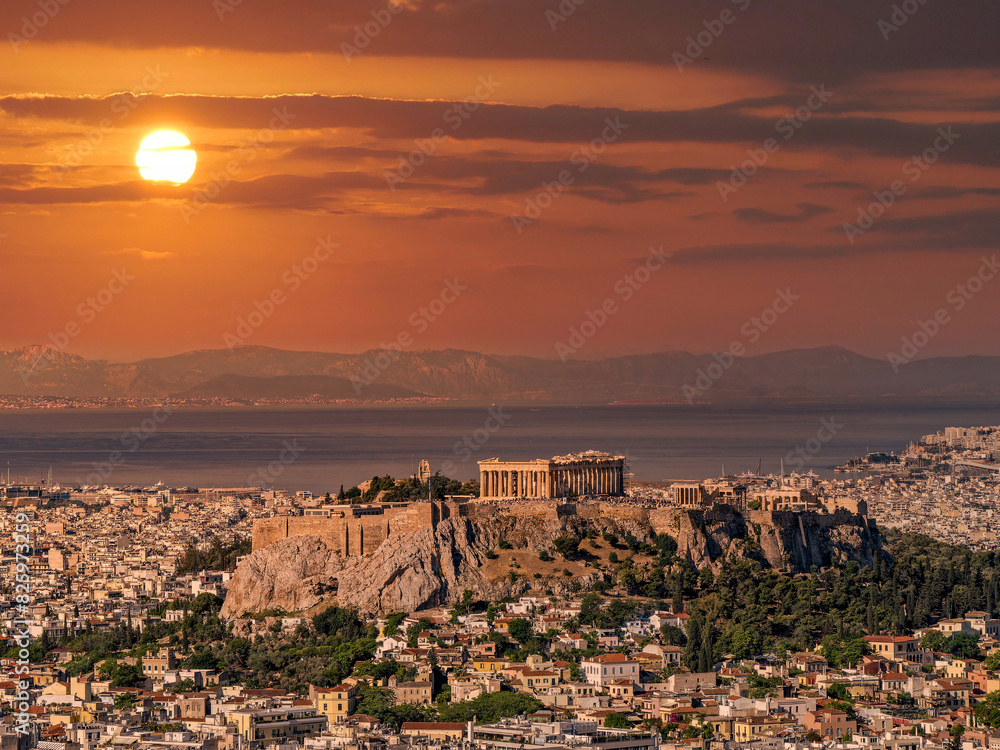 Panoramic view of Athens with Parthenon on the Acropolis and the Saronic sea in the background under a fiery sky. Travel to Greece.
