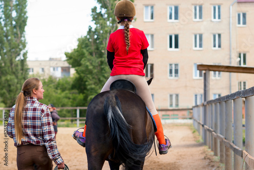 Instructor leads young rider on horse during outdoor training.