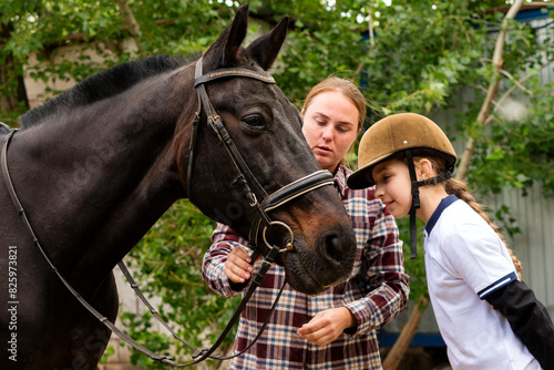 Woman and young rider during bridle adjustment on horse.