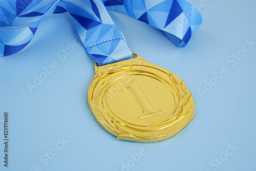 Close up of gold medal with blue ribbon on blue background.