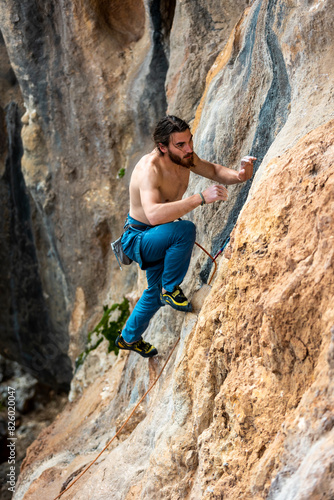 young sporty male climber with long hair climbs a rock. muscular young man. a man climbs a very difficult route. extreme sport.