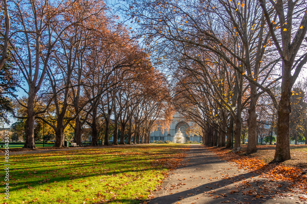 Beautiful autumn trees in soft sunlight adorn Carlton Gardens, water fountains and the historic Royal Exhibition Building in the distance. The park is a tourist attraction in Melbourne Australia