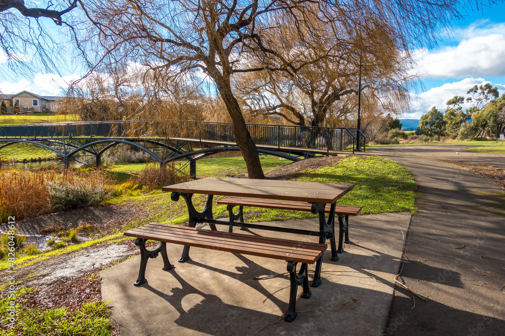 Picnic table on the beautiful riverbank of Elizabeth River with autumn trees and a footbridge at Campbell Town. Tasmania, Australia