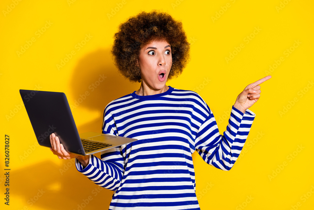 Portrait of astonished girl with perming coiffure hold laptop look directing at promo empty space isolated on yellow color background Portrait of astonished girl with perming coiffure hold laptop look directing at promo empty space isolated on yellow color background