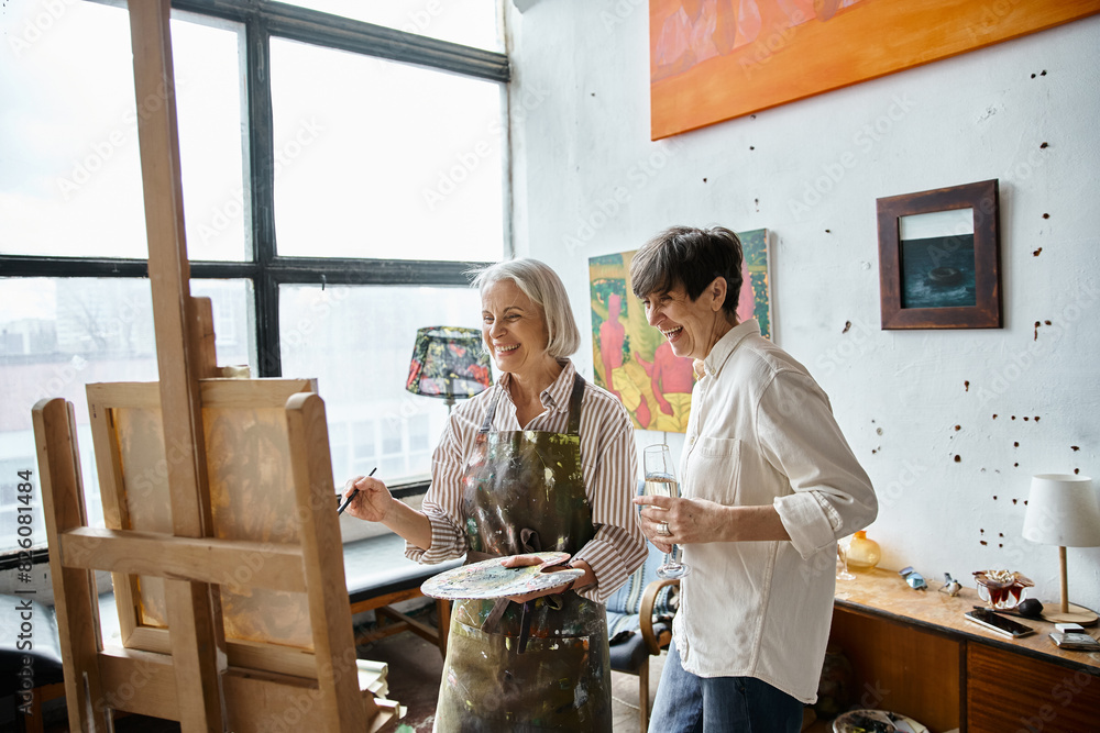 Two women, mature and in love, stand together in an art studio. Two women, mature and in love, stand together in an art studio.